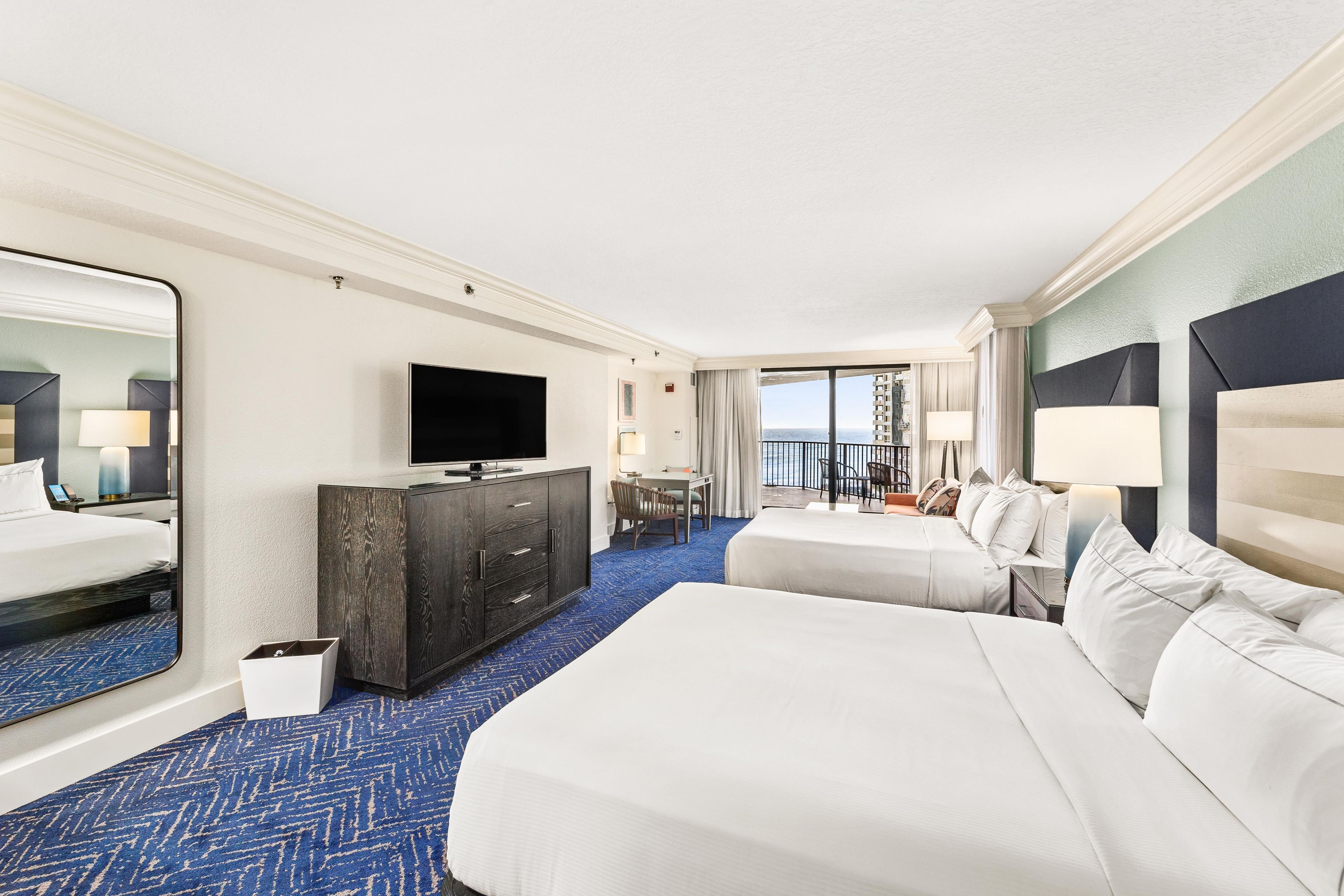 Une chambre d’hôtel avec deux lits, une télévision, un minibar et un balcon avec vue.