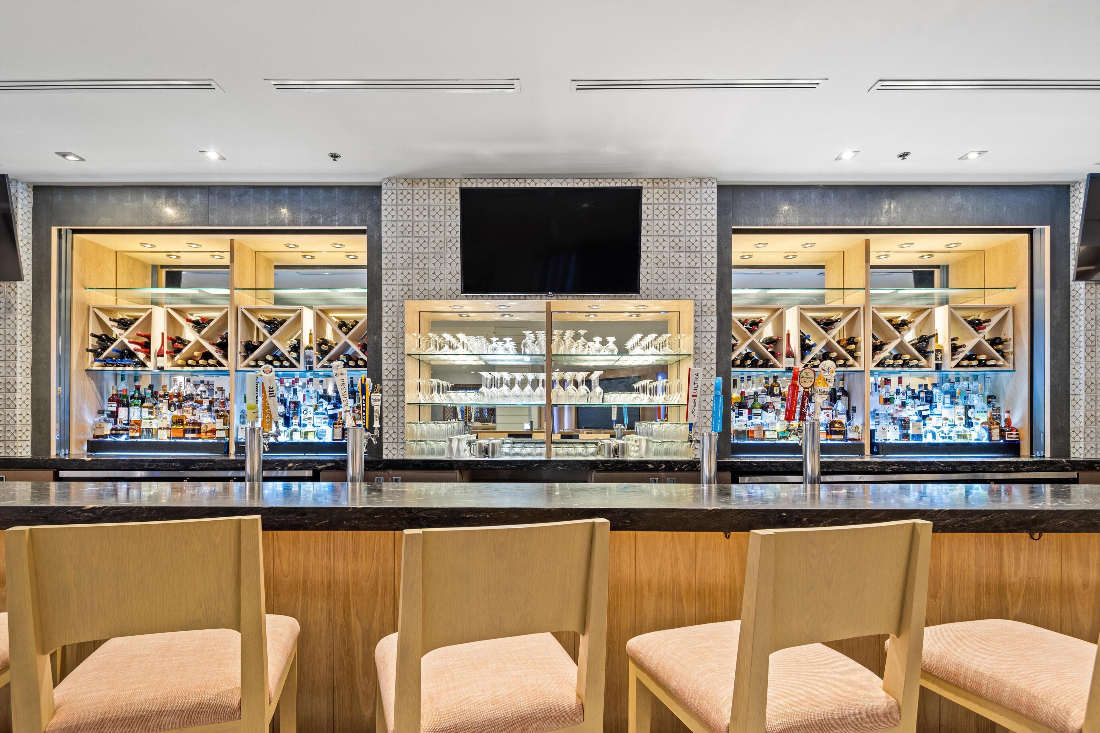 A bar area with seating, a television screen, and shelves of bottles and glasses.
