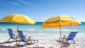 A beach scene with two blue beach chairs and two yellow umbrellas. - Hilton Sandestin Beach Golf Resort & Spa (Miramar Beach)