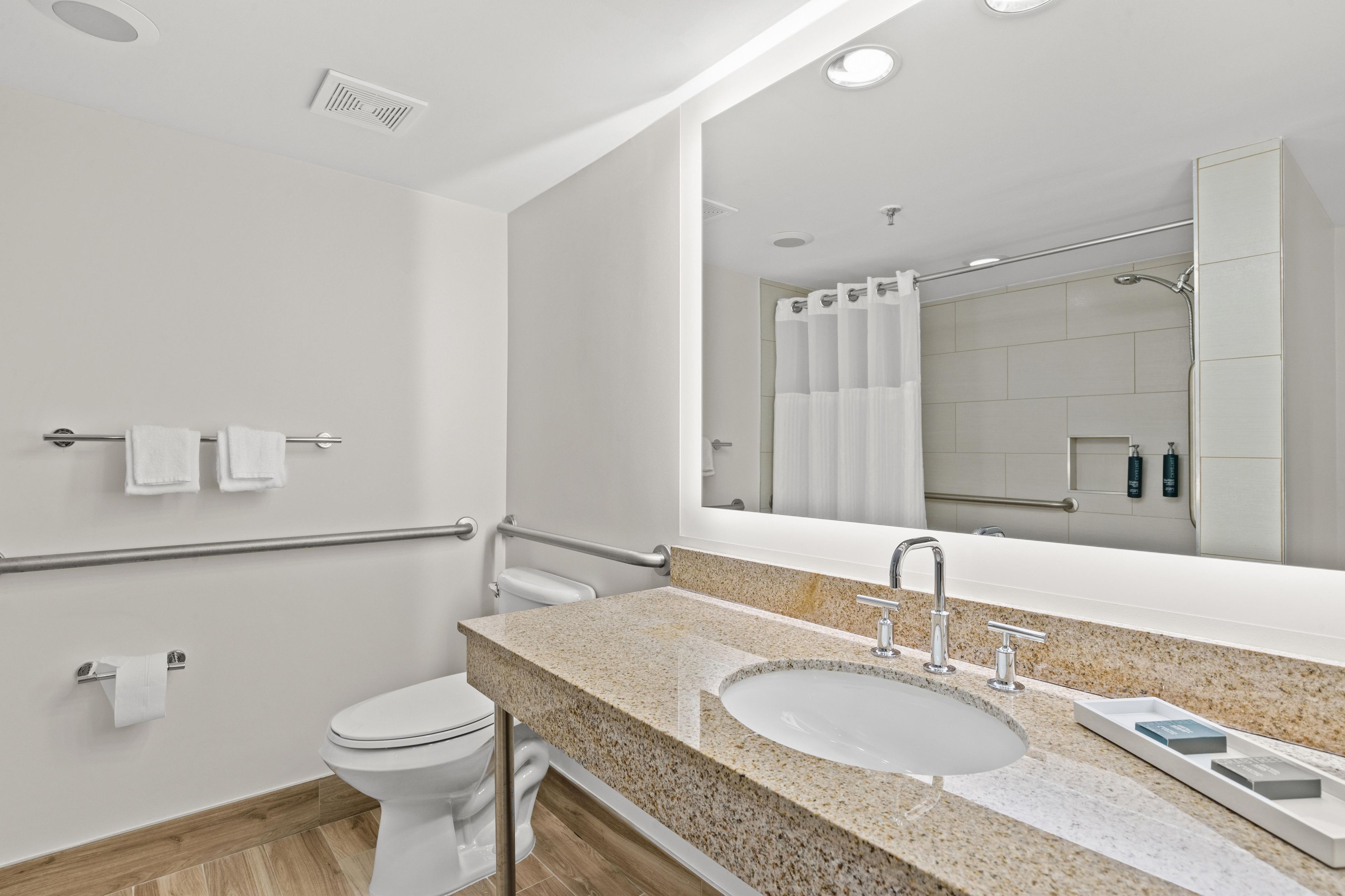 A modern bathroom with a granite countertop, a sink, a mirror, a toilet, and a shower area.