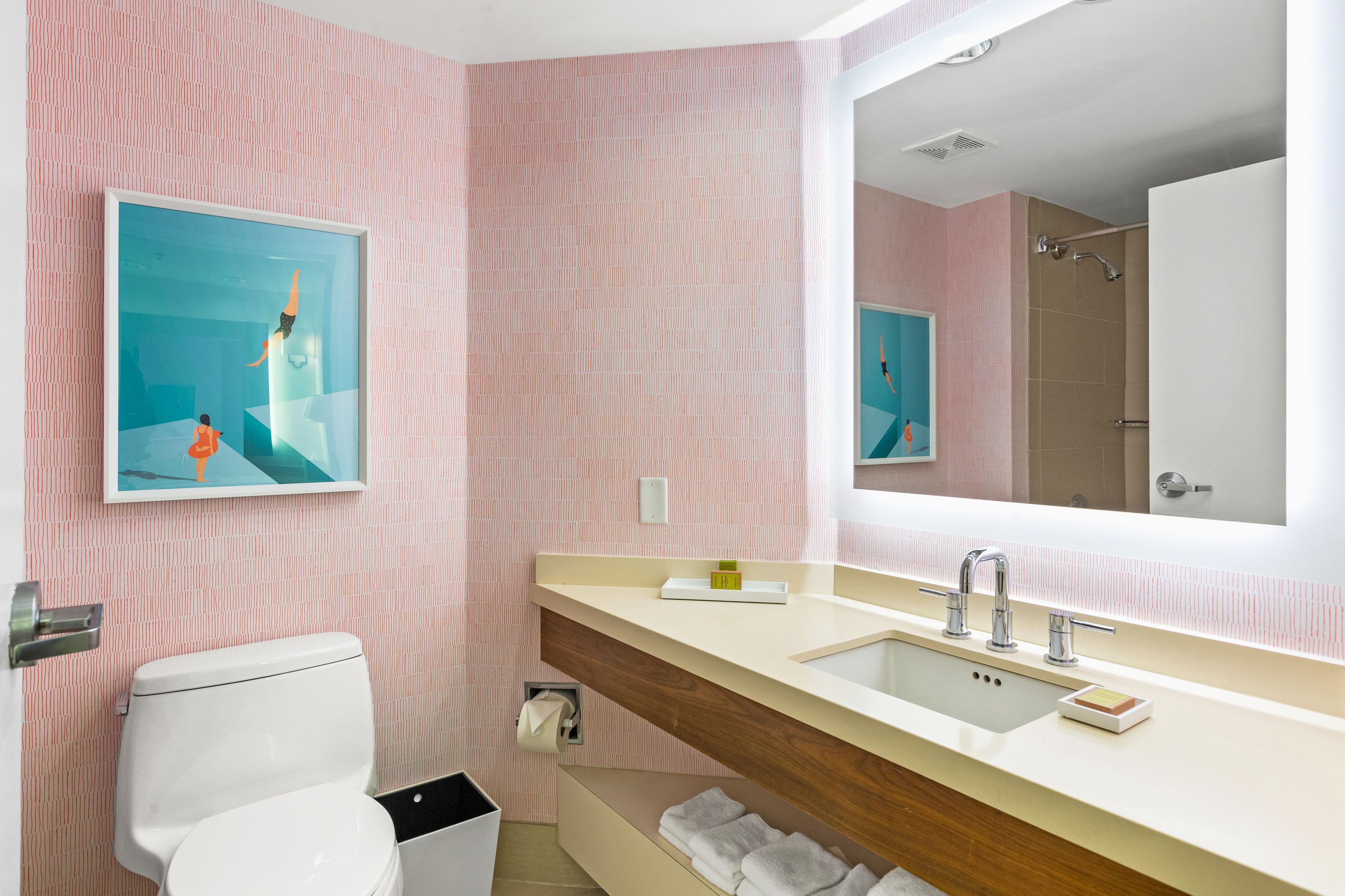 A bathroom with a toilet, sink, and a large mirror. There are two framed pictures on the wall.