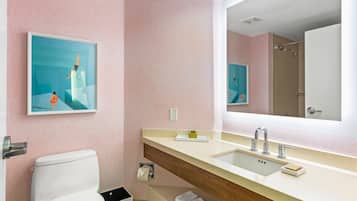 A bathroom with a toilet, sink, and a large mirror. There are two framed pictures on the wall.