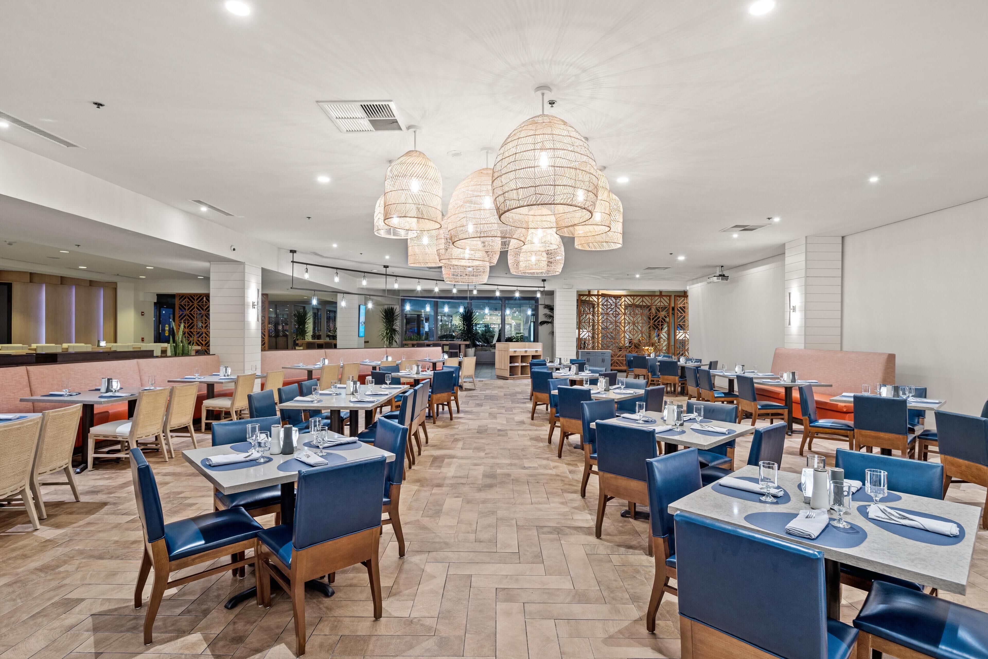 A spacious dining area with multiple tables and chairs, a central bar, and a view of the outdoor area.
