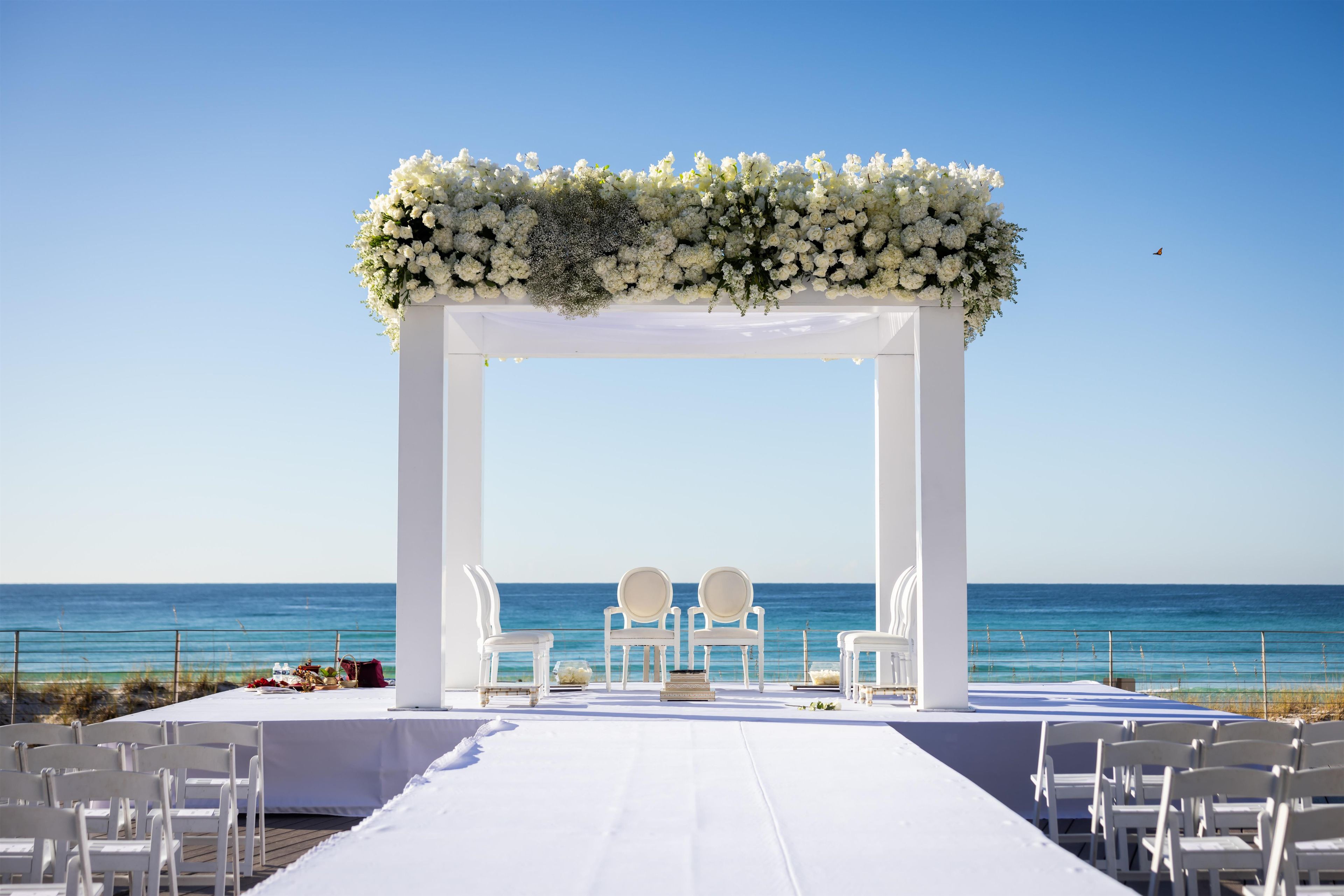 A beach wedding setup with a white arch and chairs facing the sea.
