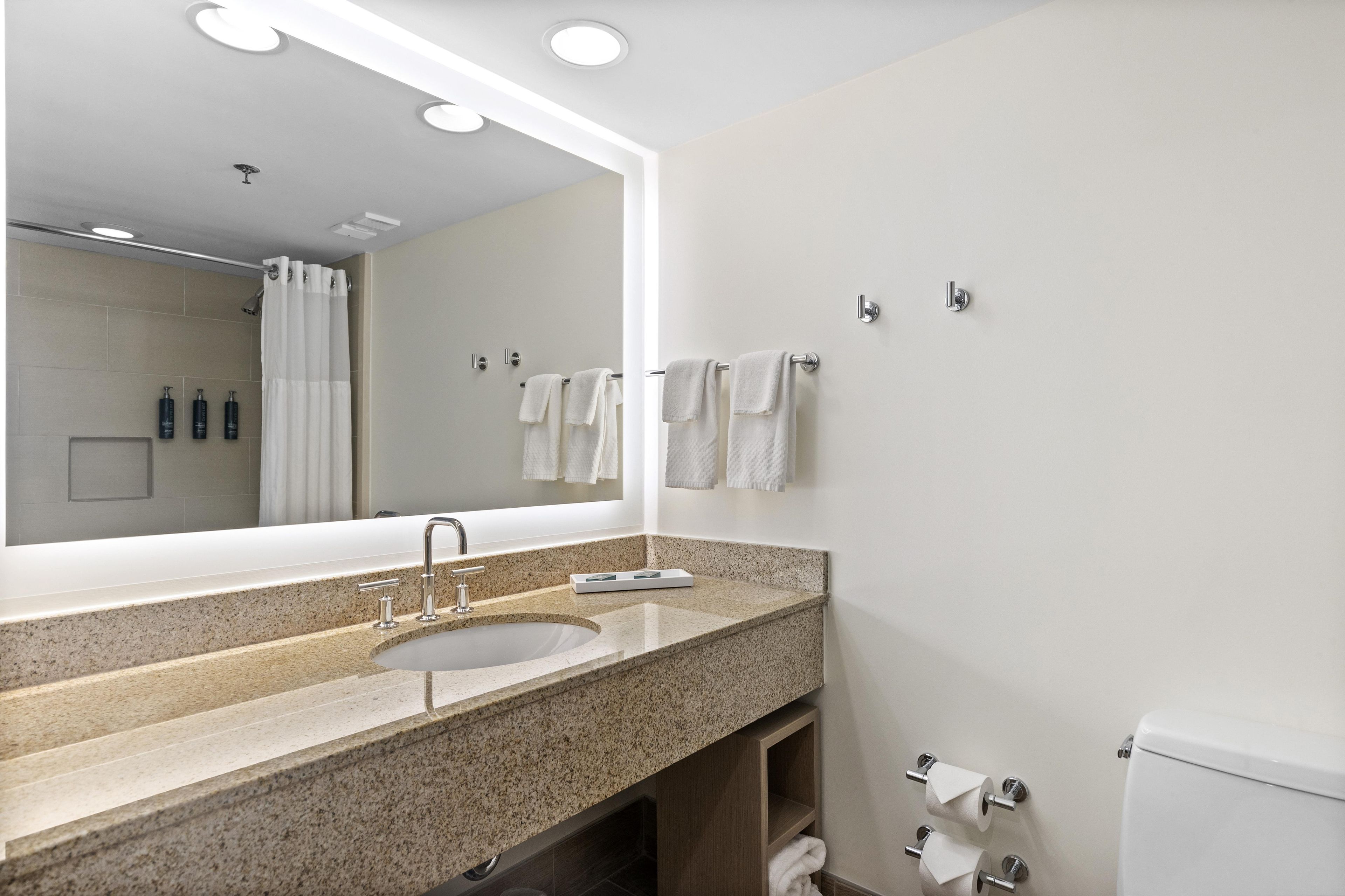 A modern bathroom with a large mirror, a sink, and a toilet.
