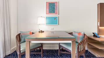 Habitación de hotel con una mesa de comedor, sillas, una lámpara, un teléfono y obras de arte en la pared.