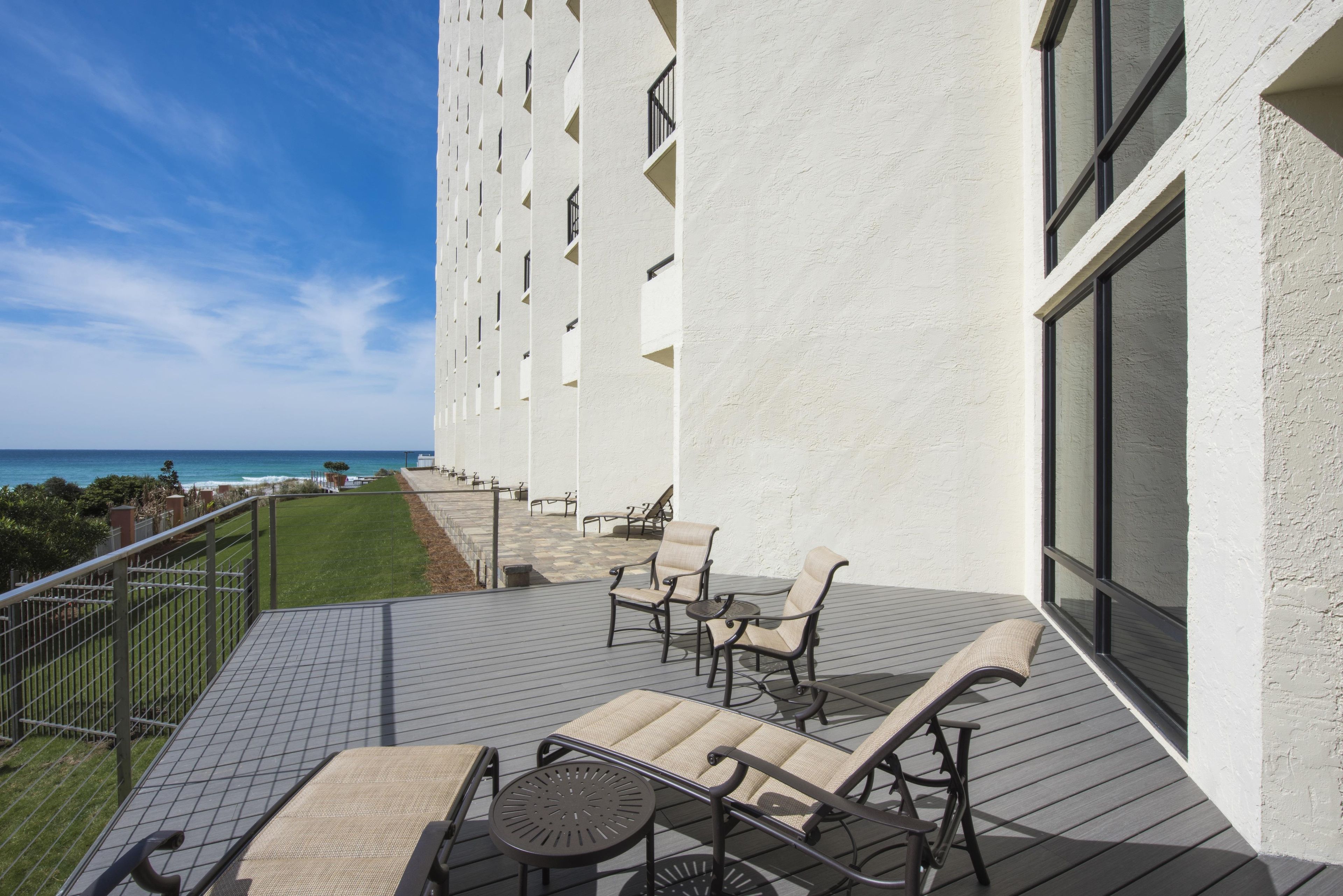 A balcony with outdoor furniture, a view of the ocean, and a building with a white facade.