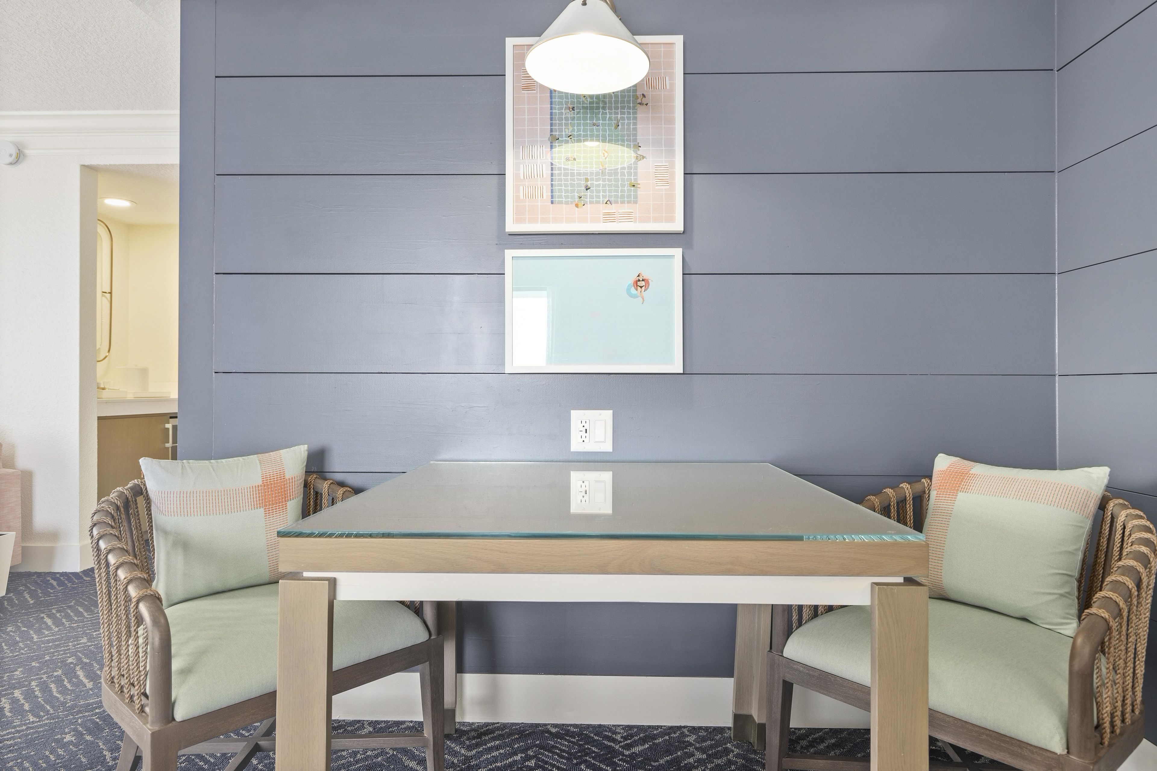Uma área de jantar com mesa e cadeiras, luminária fixada na parede e um quadro emoldurado.