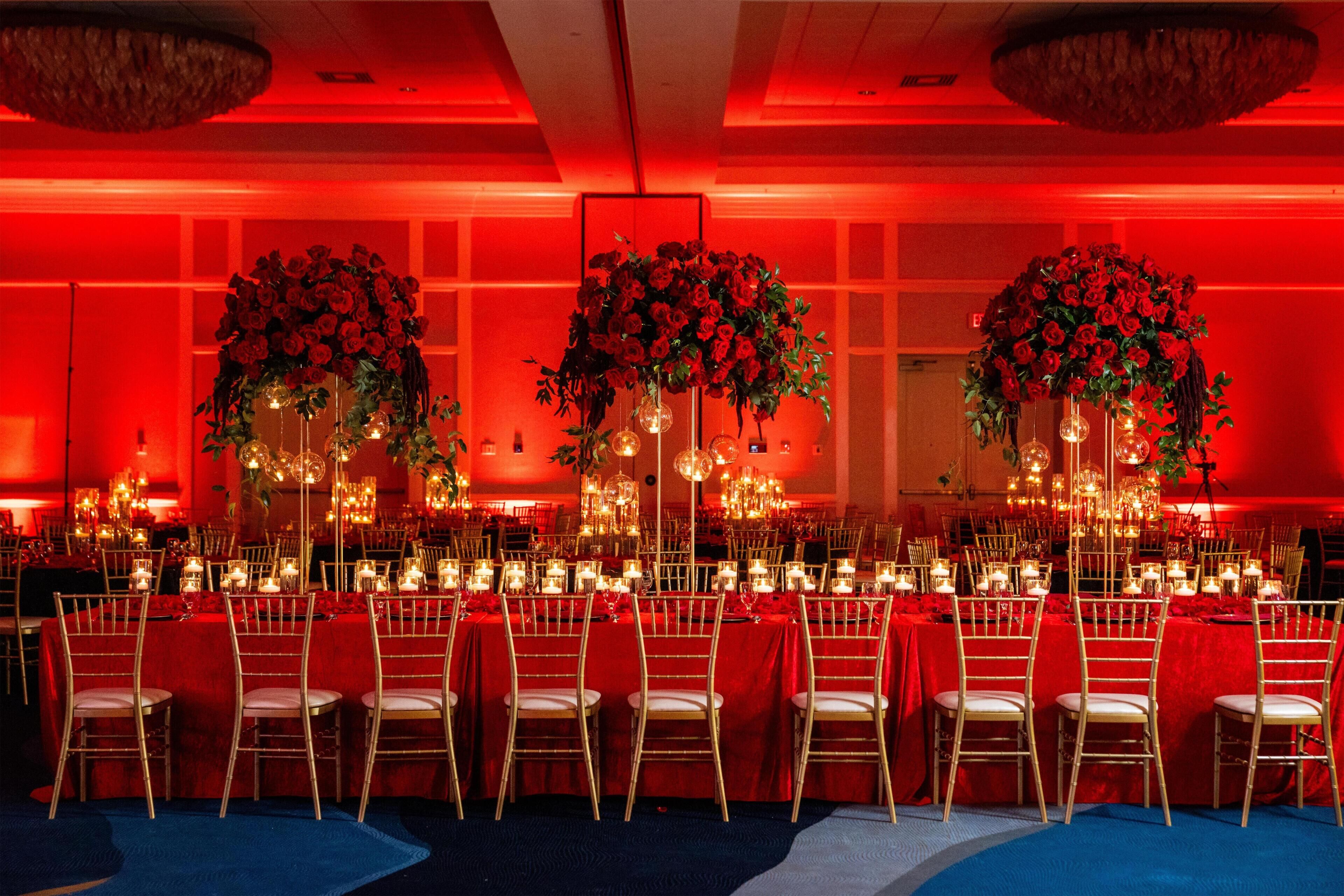 Ein Festsaal mit roten Tischen, goldenen Stühlen und floralen Tischdekorationen.