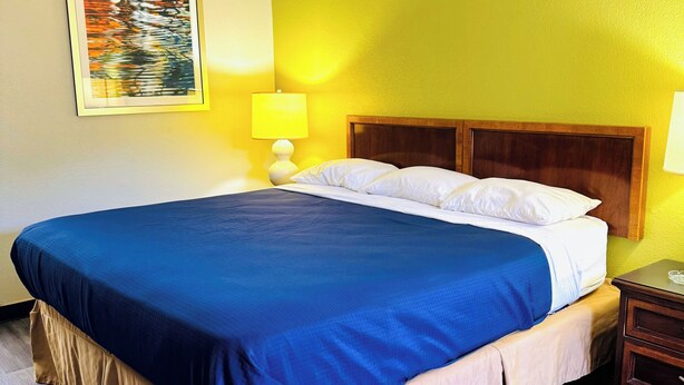 A hotel room with a large bed, wooden headboard, and a nightstand with a lamp. - Newnan Lodge (Newnan)