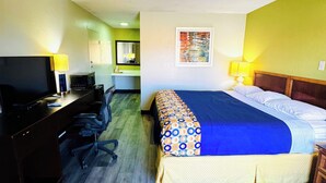 A hotel room with a bed, desk, chair, television, and a bathroom visible in the background. - Newnan Lodge (Newnan)