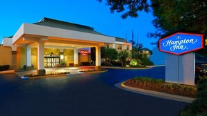 A Hampton Inn hotel with a well-lit entrance, a signboard, and a parking area.