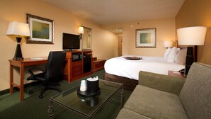 A hotel room with a bed, a desk with a computer, a chair, a coffee table, and a TV.