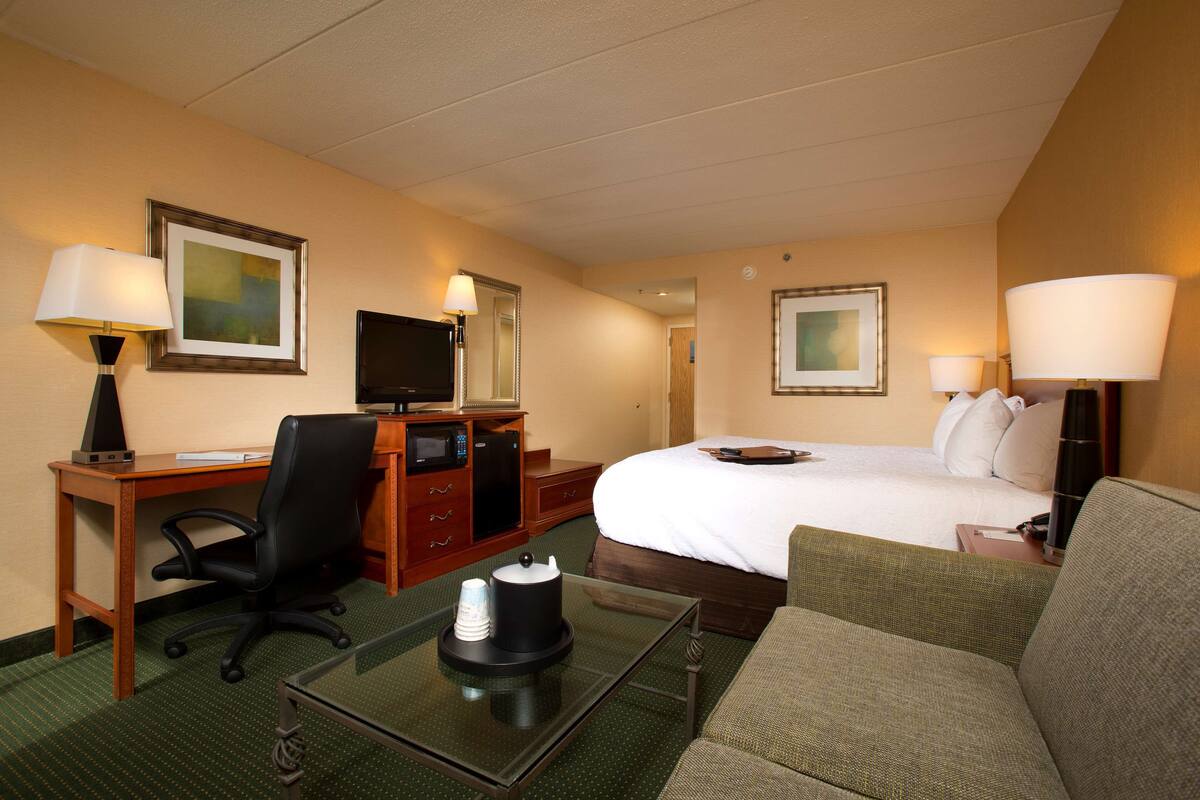 A hotel room with a bed, a desk with a computer, a chair, a coffee table, and a TV.