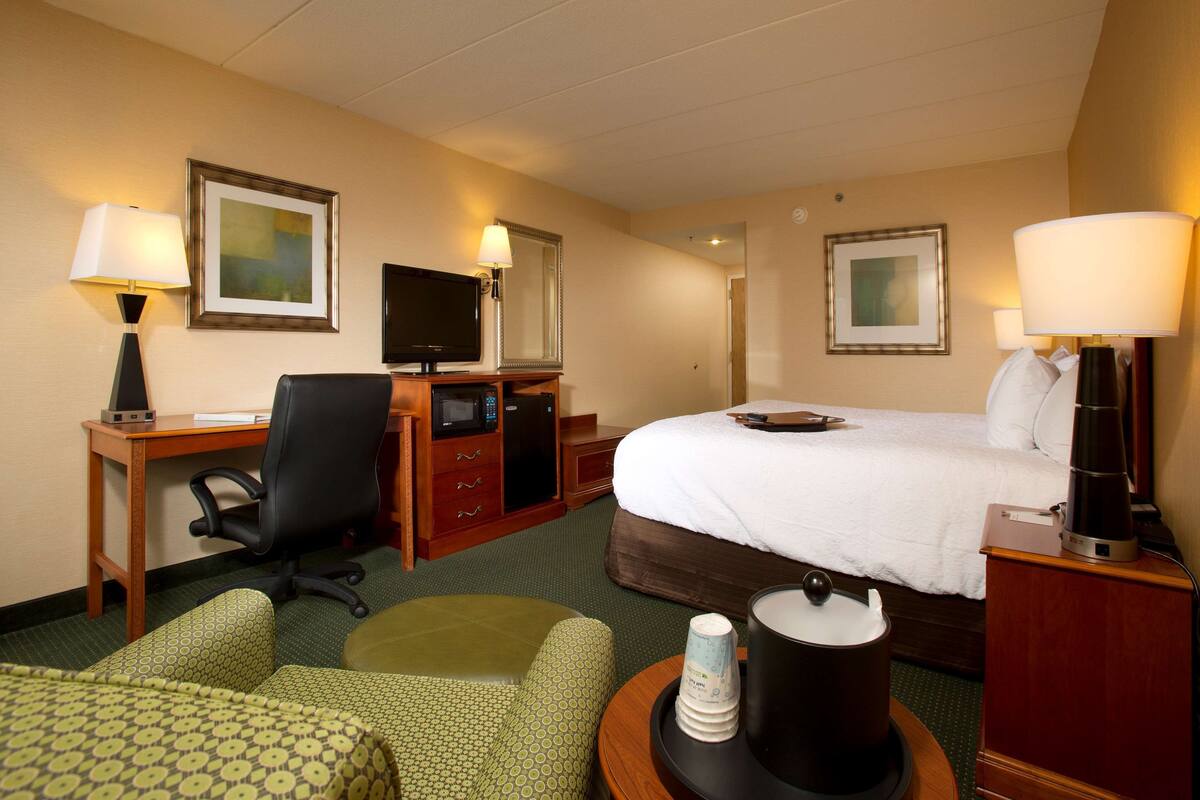 A hotel room with a bed, desk, chair, television, and lamps.