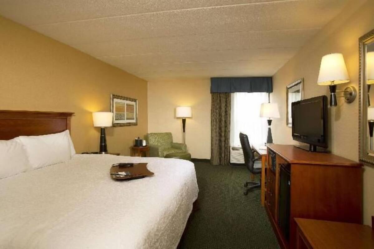 A hotel room with a large bed, a desk with a television, a chair, and two lamps.