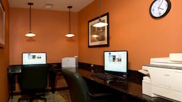 A hotel reception area with two computer workstations, a clock, and a printer.