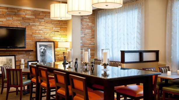 A dining area with a brick wall, a large flat-screen TV, and a dining table with chairs.
