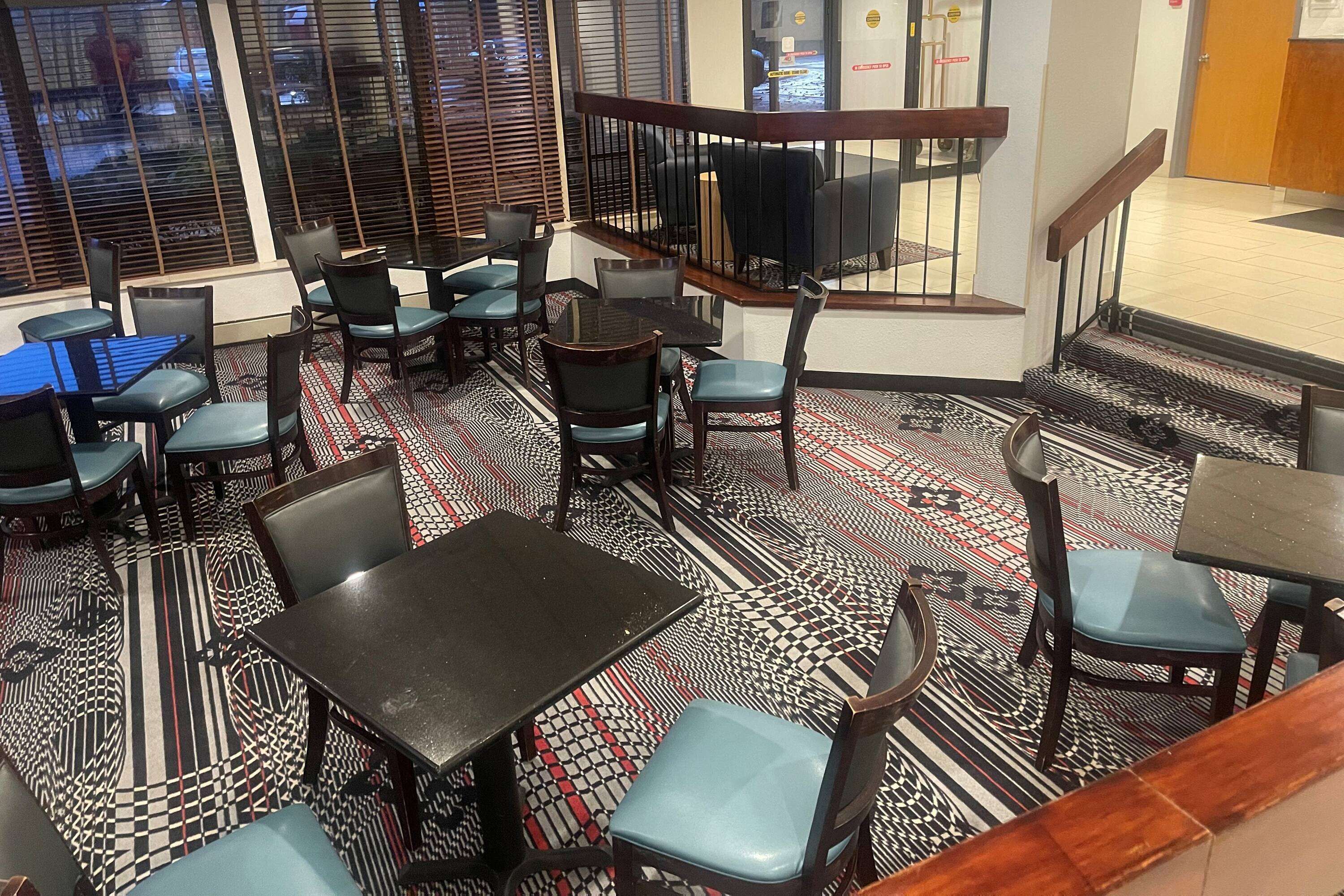 A restaurant with tables and chairs, a patterned floor, and a staircase.
