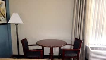 A hotel room with a bed, a round table with two chairs, a lamp, and a window with curtains.