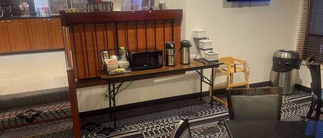Una habitación de hotel con kitchenette, televisor montado en la pared, piso estampado y un pequeño rincón de descanso.