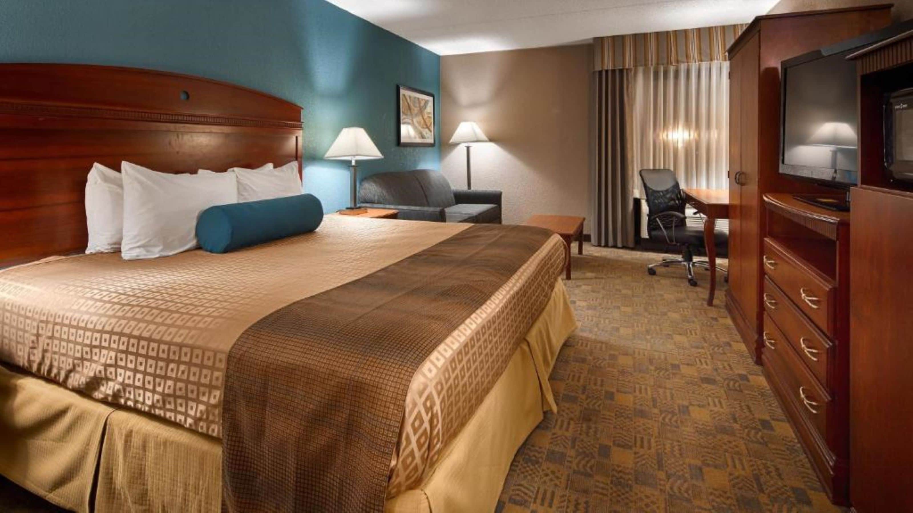 A hotel room with a large bed, a desk, a chair, a TV, and a wardrobe.