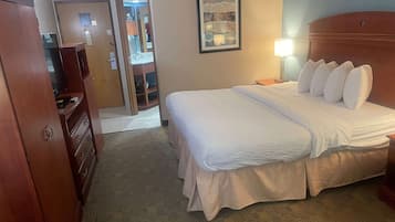 A hotel room with a neatly made bed, a wooden dresser, and a door leading to a bathroom.