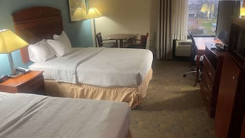 A hotel room with two beds, a desk with a chair, a television, and a window with a view of the outside.