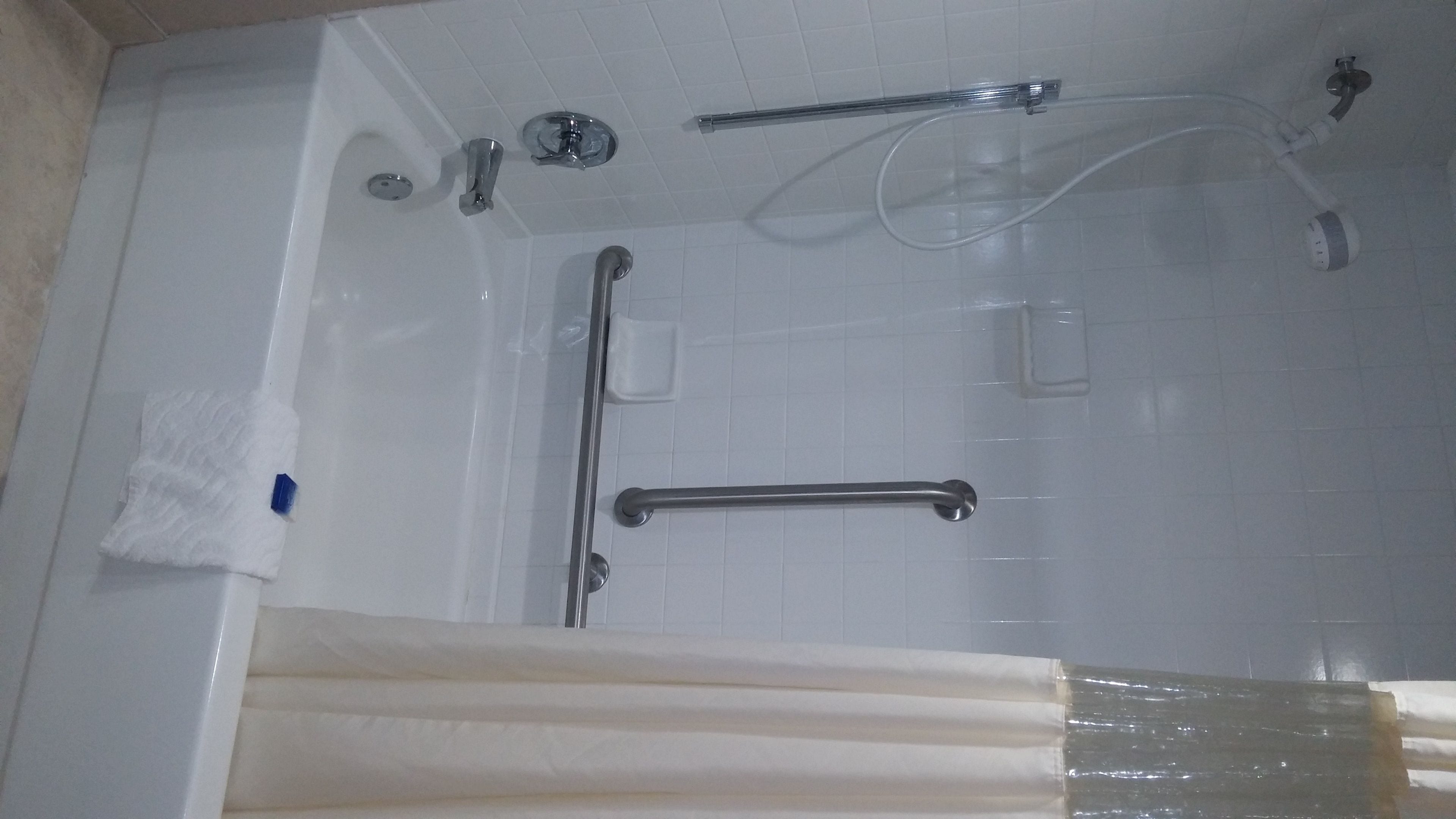 Una bañera con cabezal de ducha manual, barras de apoyo y grifo manual.