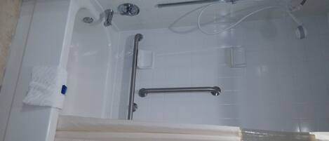 Una bañera con cabezal de ducha manual, barras de apoyo y grifo manual.
