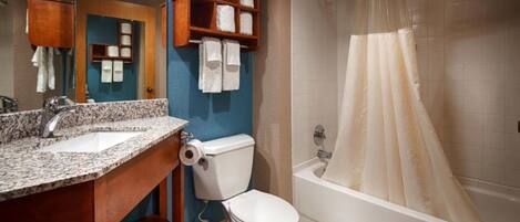 A bathroom with a granite countertop sink, a toilet, a shower with a beige curtain, and a wooden medicine cabinet with towels.