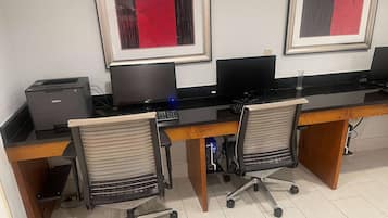Un espacio de trabajo con dos escritorios, sillas, computadoras e impresora.