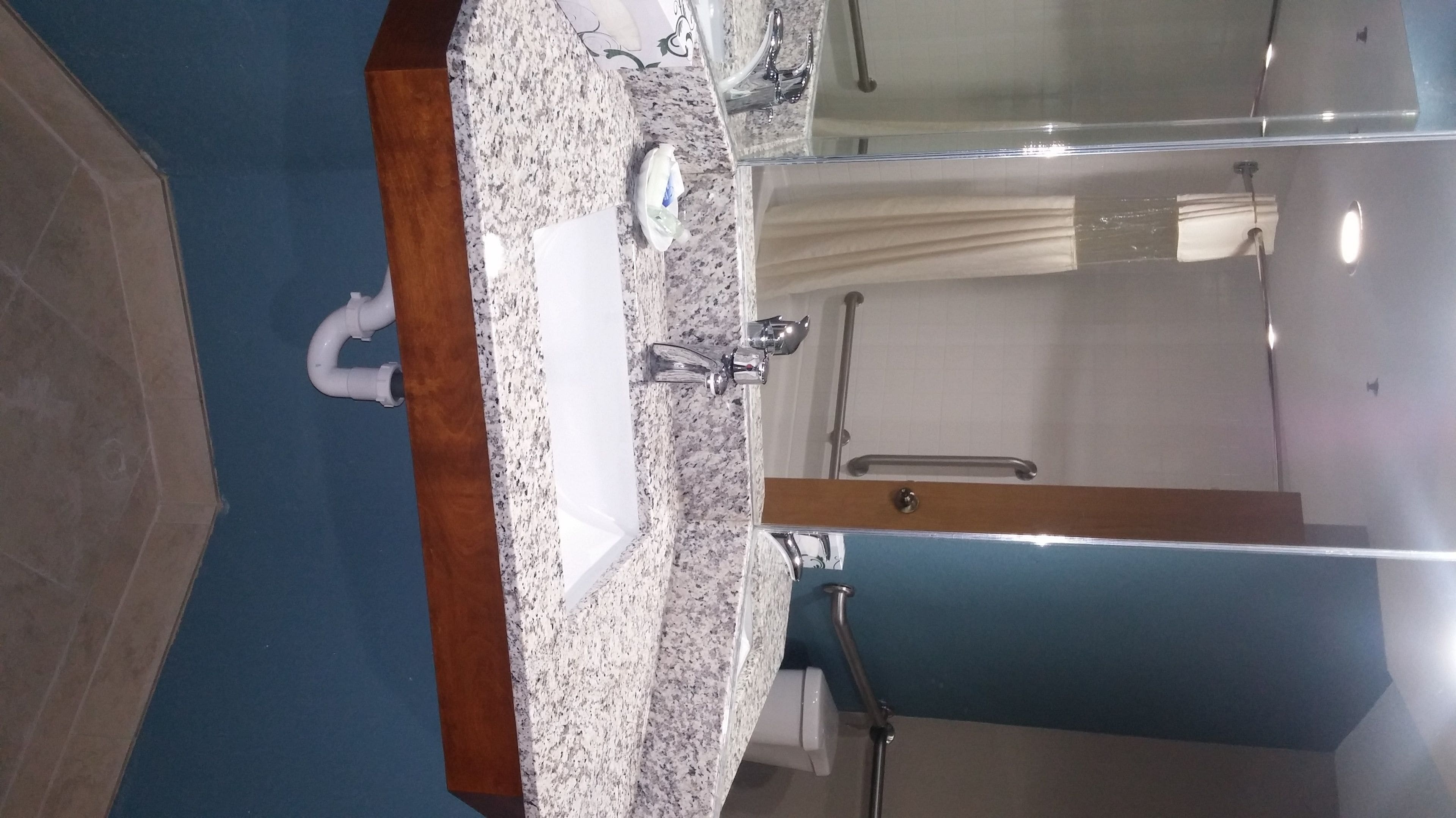 A bathroom with a granite countertop, a sink, a mirror, and a shower area.