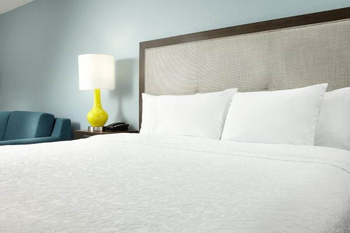 A neatly made bed with white linens, a wooden headboard, and a bright yellow bedside lamp.