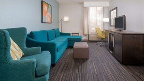Habitación de hotel con sofá color turquesa, un pequeño otoman, escritorio con televisor y una silla.