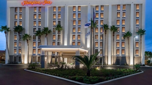 Un hotel Hampton Inn con una fachada moderna, varios pisos y una entrada bien iluminada.