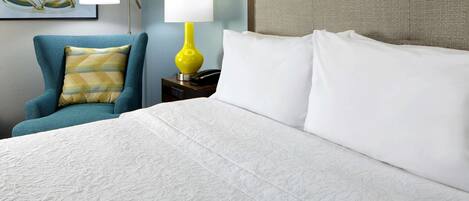 Een hotelkamer met een bed, een stoel, een nachtkastje, een lamp en een kunstwerk aan de muur.