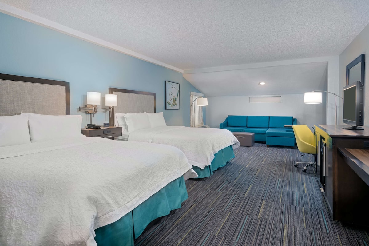 Habitación de hotel con dos camas, un escritorio con computadora, un sofá azul y una silla amarilla.