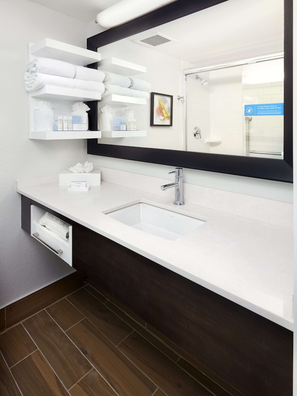 A modern bathroom with a white sink, dark wood vanity, and a mirror above the sink. There are towels and toiletries on the shelves. - Hampton Inn Orlando Near Universal Blv/International Dr (Orlando)