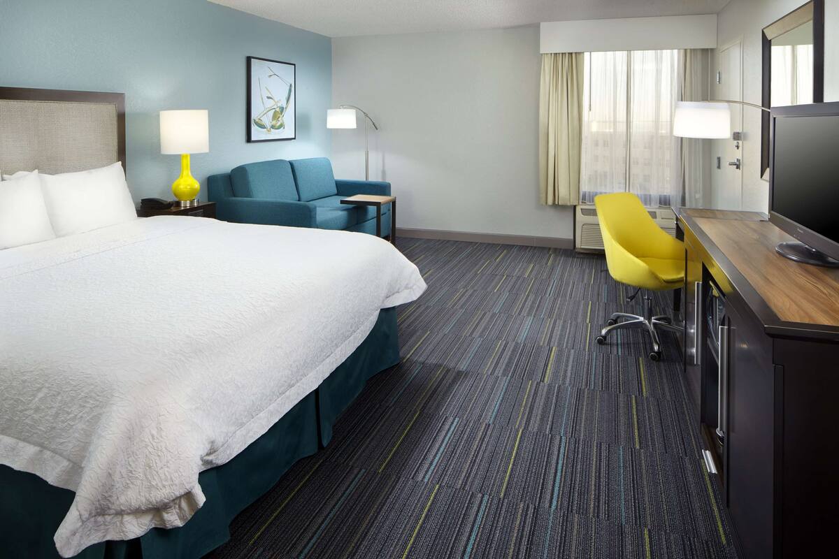 Una habitación de hotel con cama, escritorio con silla, televisor y lámpara.