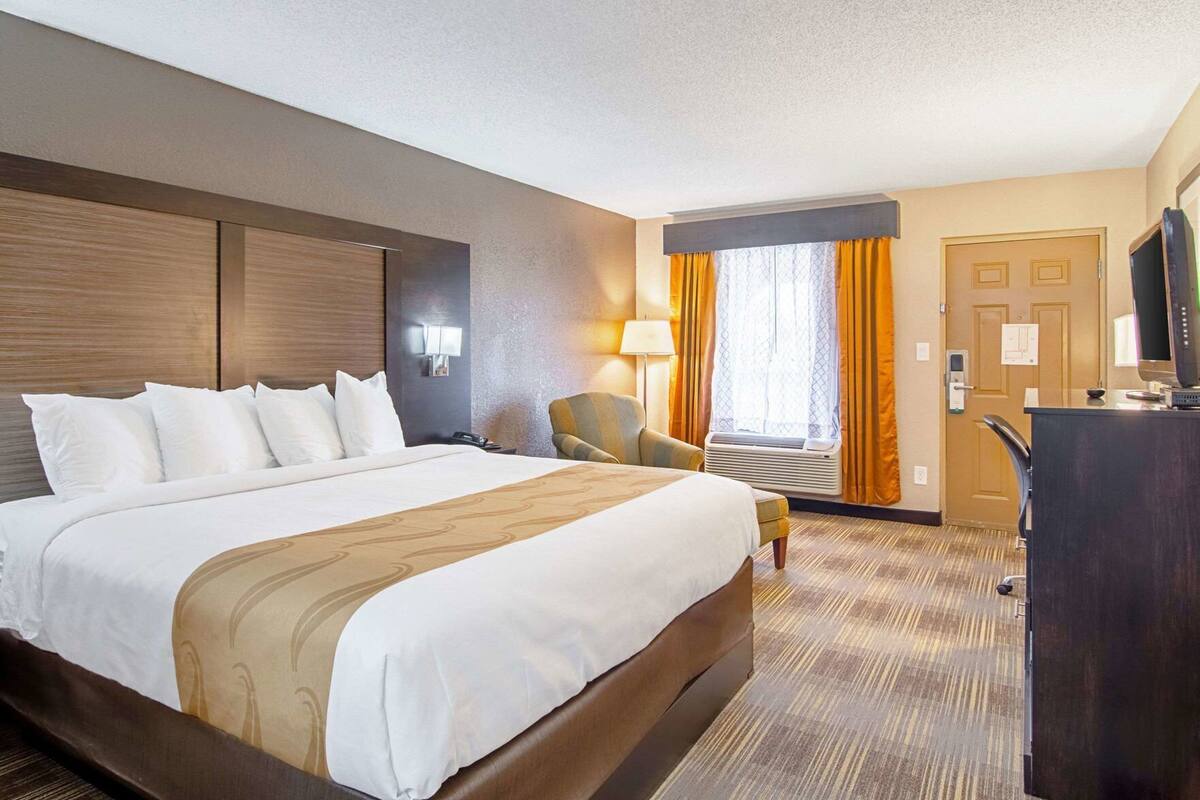 A hotel room with a large bed, a desk, a chair, a lamp, and a window with curtains.