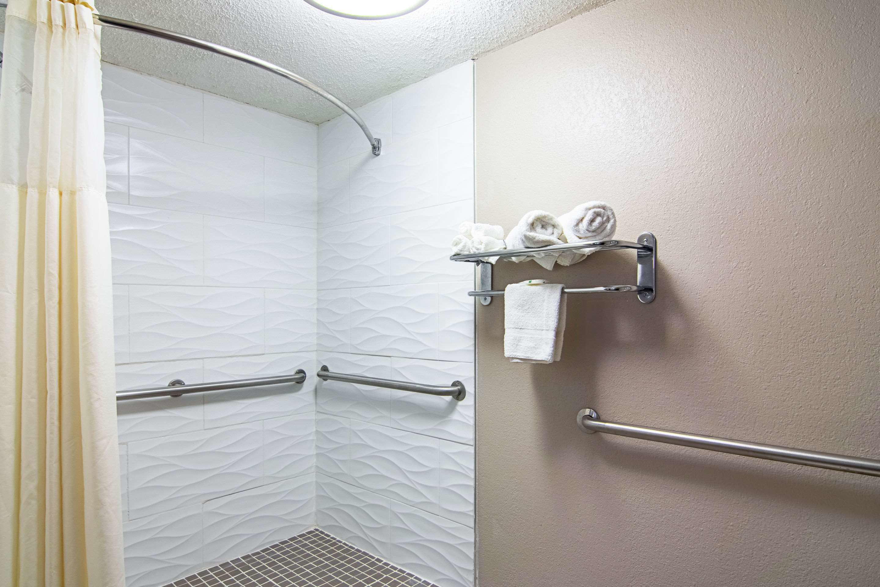 Une douche avec un mur texturé, un porte-serviettes avec des serviettes et une barre d’appui.