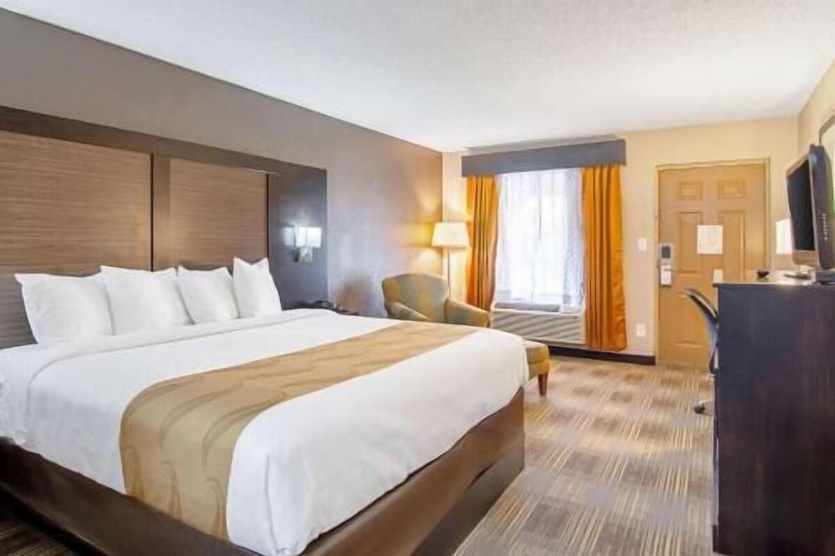 A hotel room with a large bed, a desk, a chair, and a television.