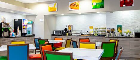 A modern restaurant with colorful chairs and tables, a counter with food and drink options, and a clean, well-lit interior.