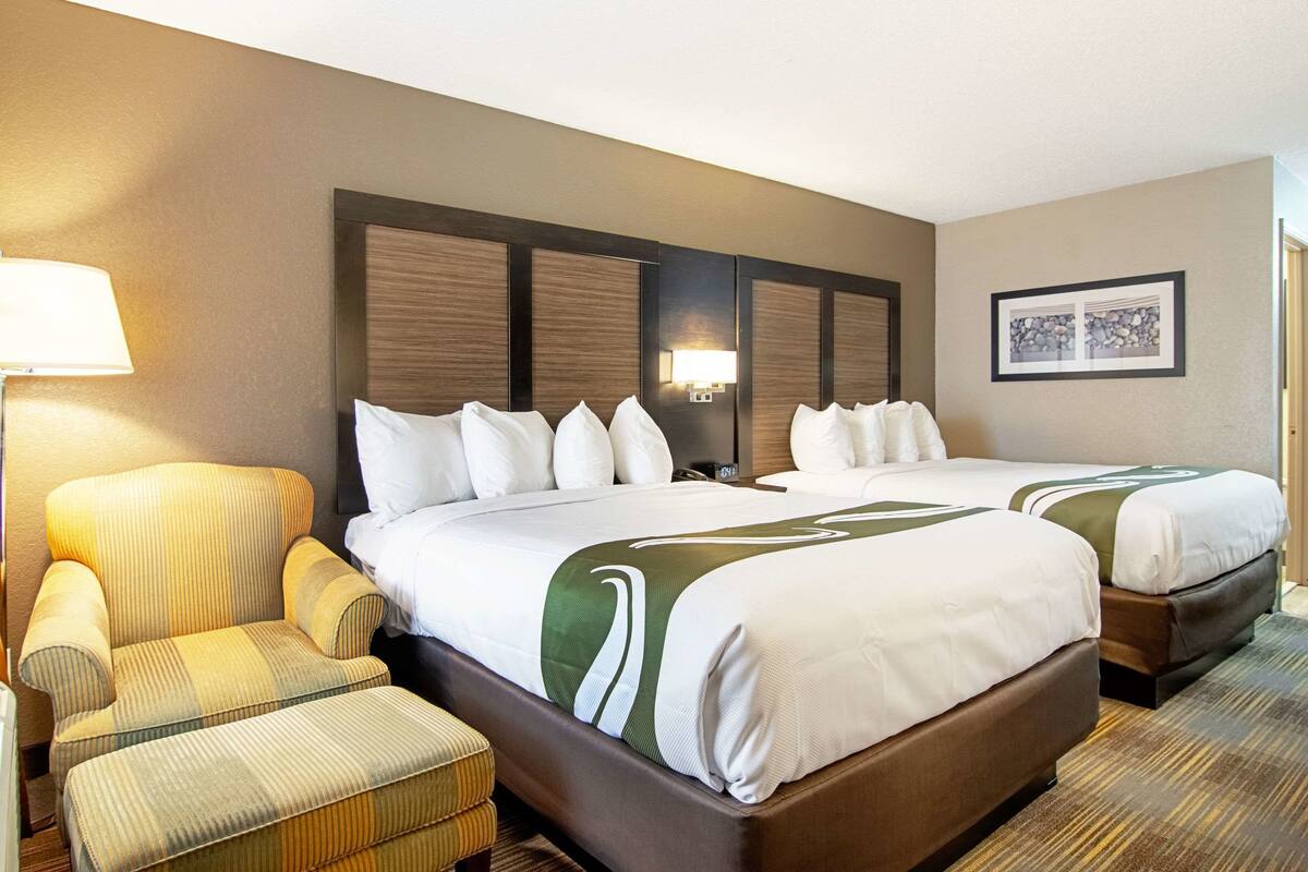 A hotel room with two beds, a chair, a lamp, and a framed picture on the wall.