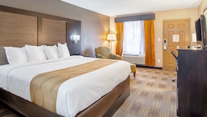 Une chambre d’hôtel avec un grand lit, un bureau, une chaise, une télévision et une fenêtre avec des rideaux.