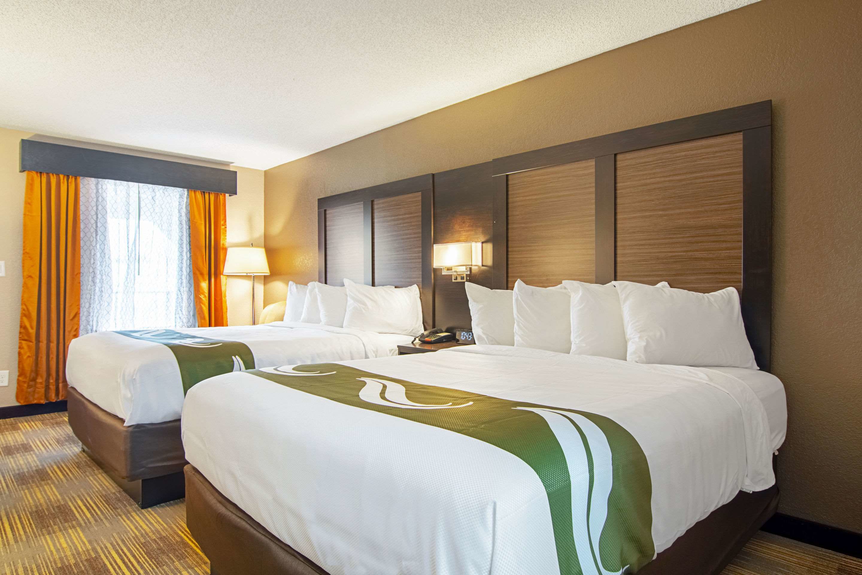 Habitación de hotel con dos camas, un ventanal con cortinas, una lámpara de pared y piso cubierto de alfombra.