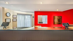 Un área de recepción de diseño moderno, con una pared de acento roja, un reloj, certificados enmarcados y un separador de vidrio.