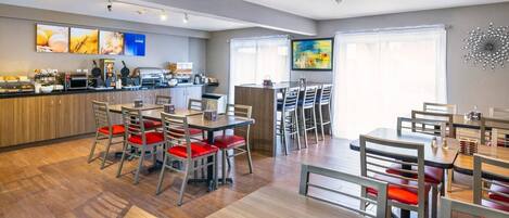 A modern dining area with wooden flooring, metal chairs with red cushions, and a central island with a kitchen counter.
