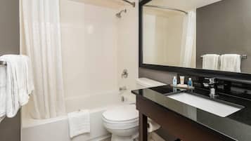 Un baño moderno con bañera, inodoro y un espejo grande.